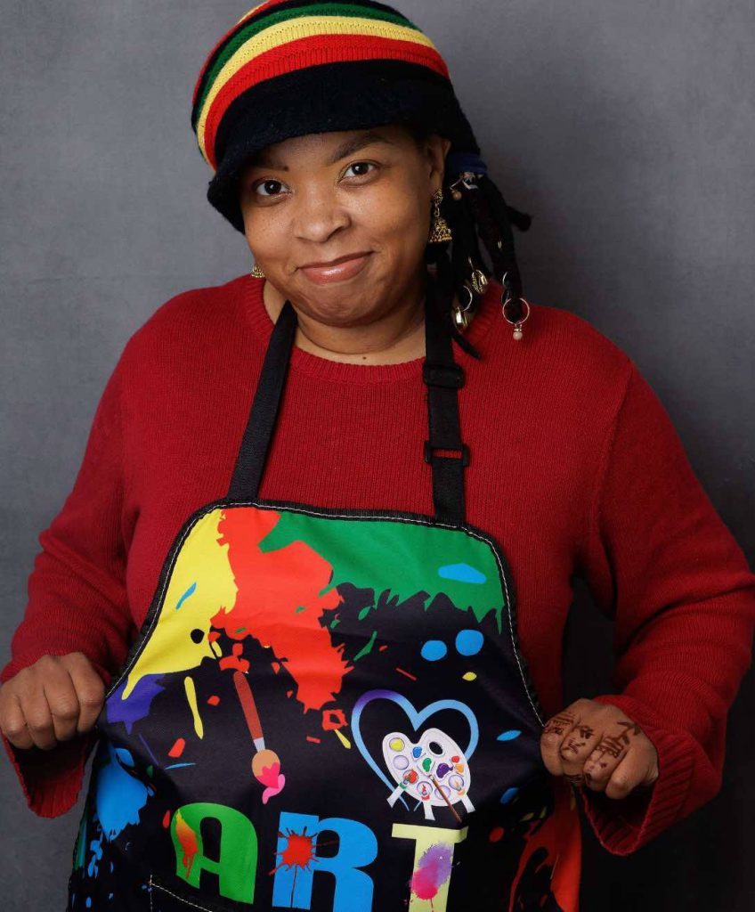 African American woman wearing a hat, a red shirt and a multi-colored apron