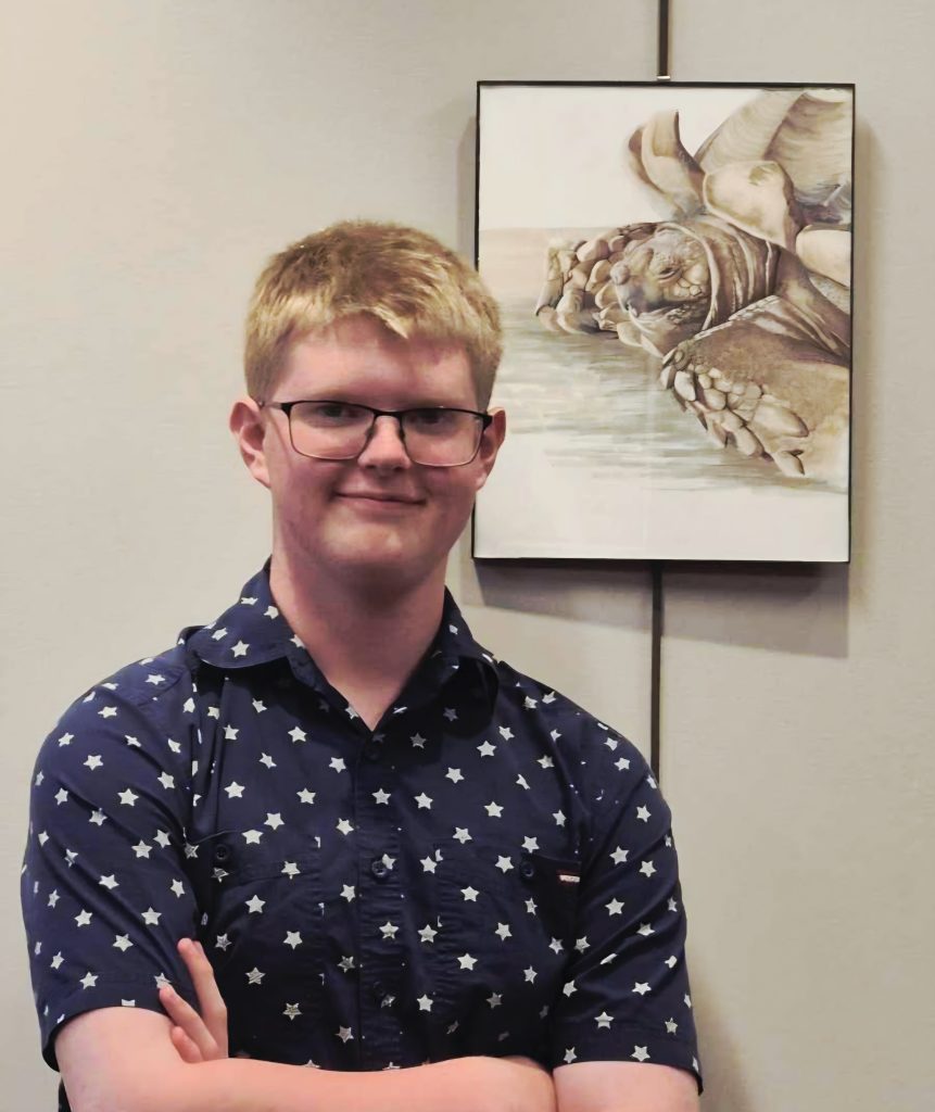 Young man standing by artwork of a turtle on a wall.