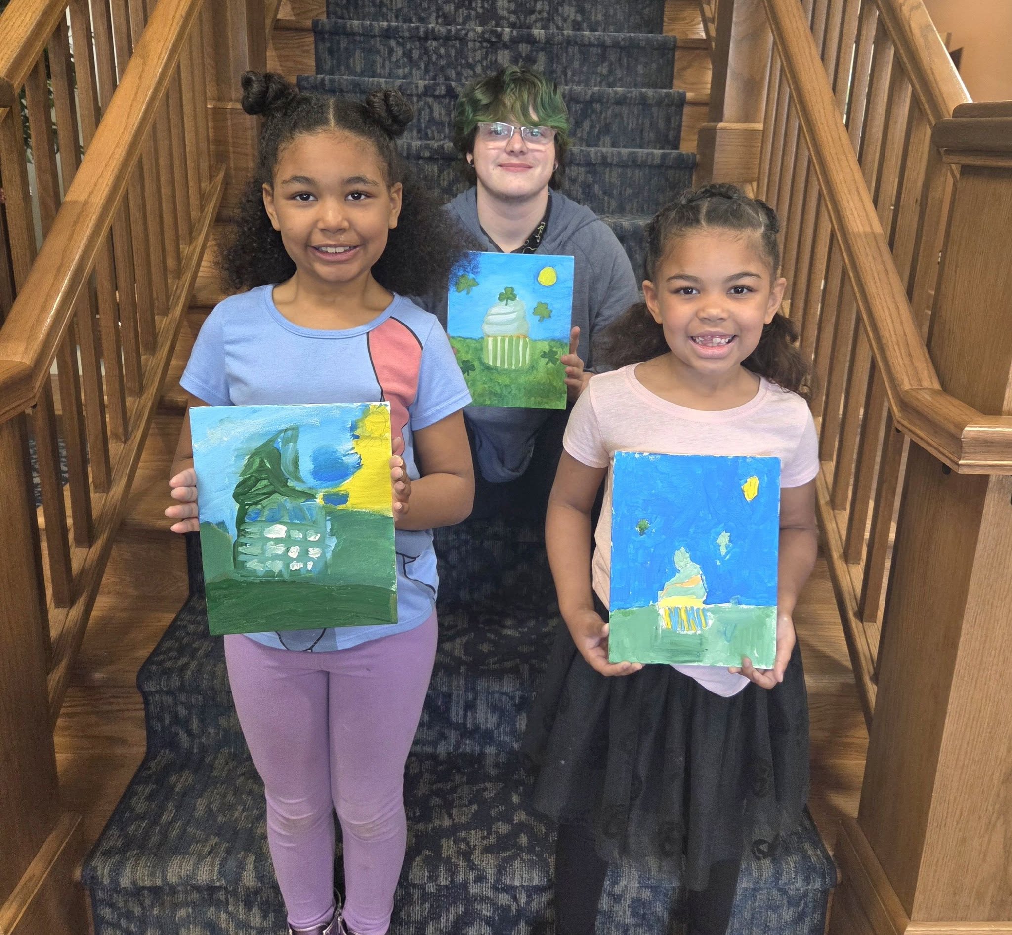 image of 2 young girls and one man sitting and standing on stairs holding art.
